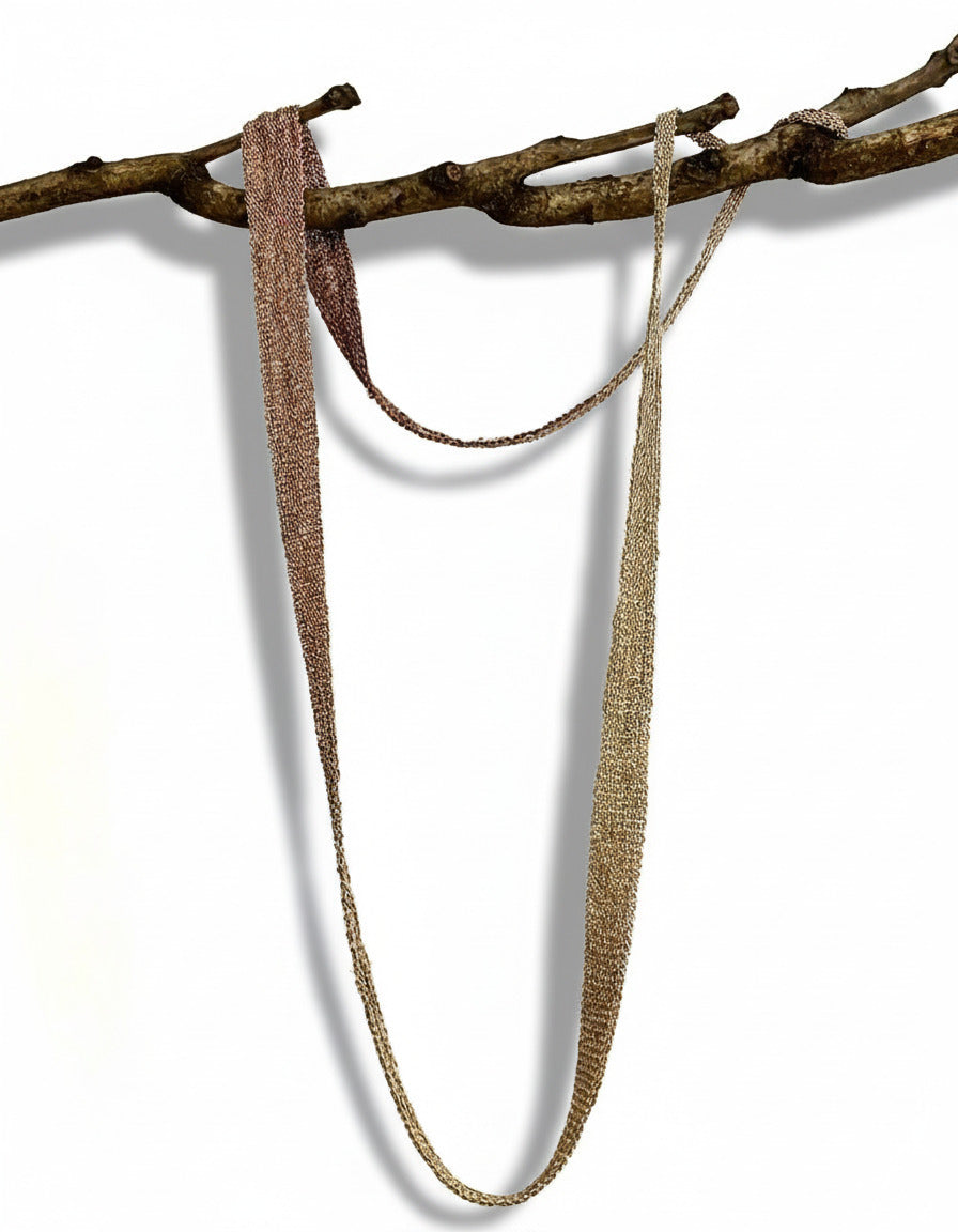 Long collier mordoré, en forme de ruban dégradé composé de chaîne d'argent patiné et fil de soie. Bijou présenté sur une branche d'arbre.