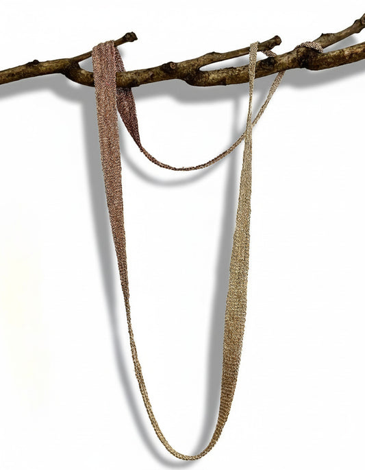 Long collier mordoré, en forme de ruban dégradé composé de chaîne d'argent patiné et fil de soie. Bijou présenté sur une branche d'arbre.