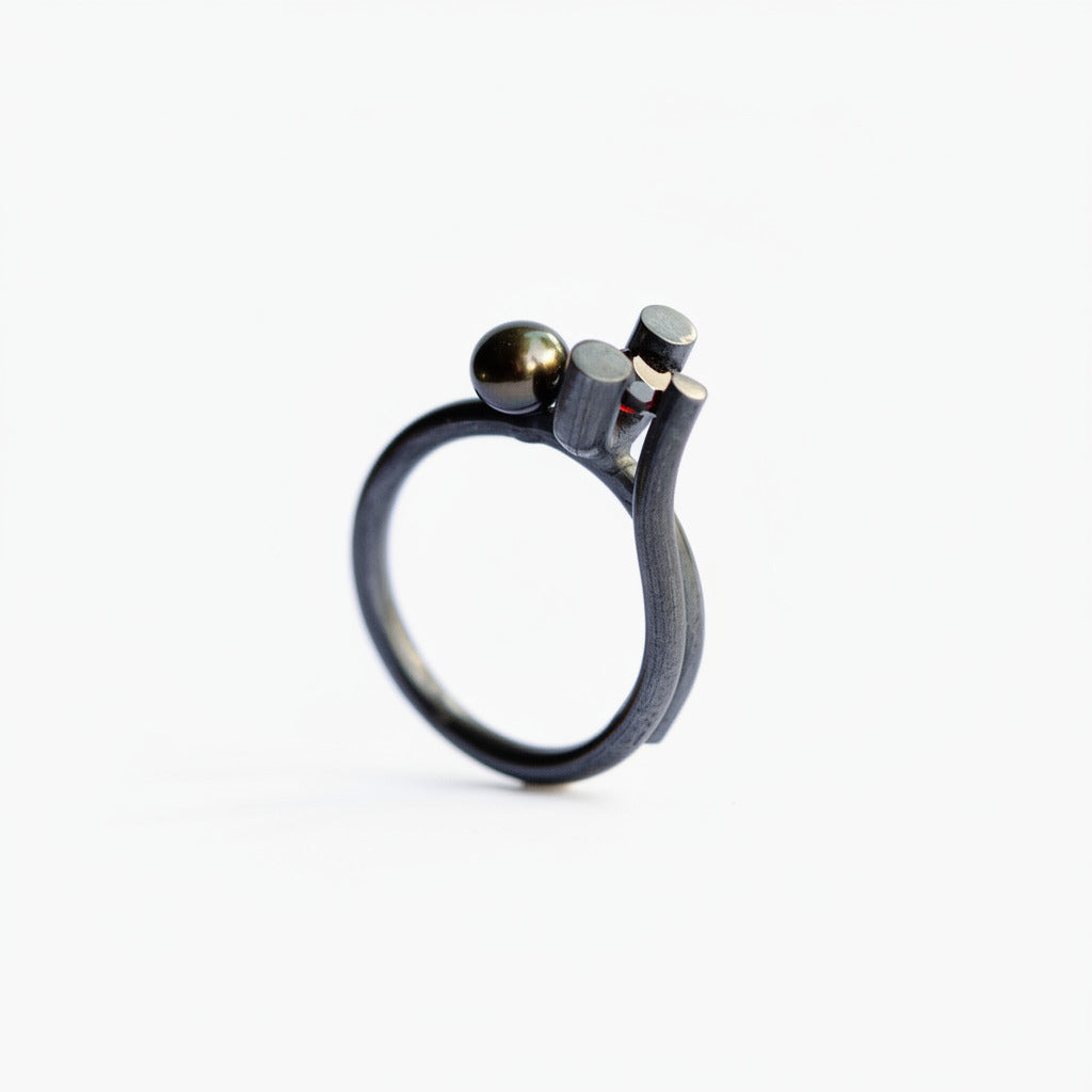 La bague Offshoot associe l’argent oxydé à une perle noire et un grenat, dans une composition graphique aux lignes organiques.