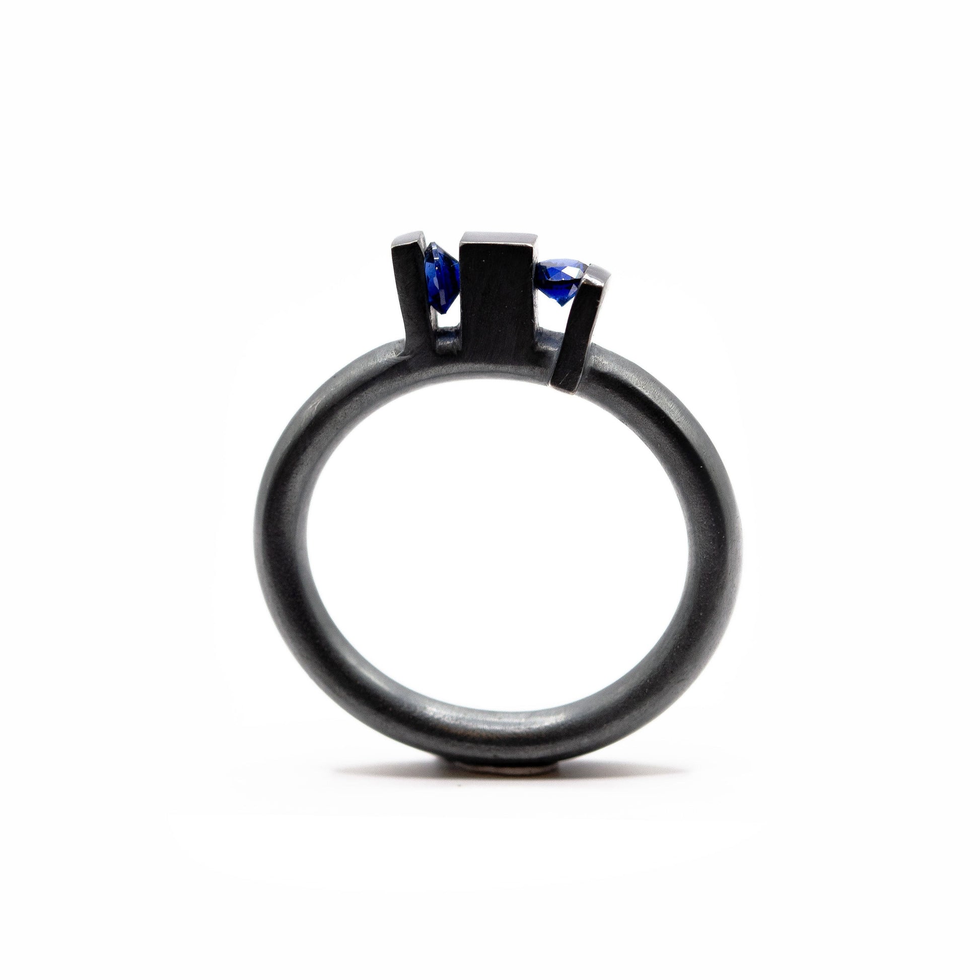 Bague contemporaine en argent forgé et oxydé avec anneau rond et volumes verticaux sculpturaux, sertie de deux saphirs de culture bleus.