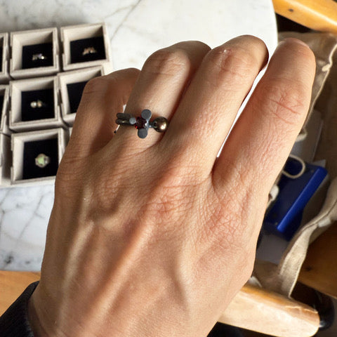La bague Offshoots s'inspire de la manière dont les plantes se développent. En argent oxydé, elle est sertie d'une perle noire et d'un grenat.