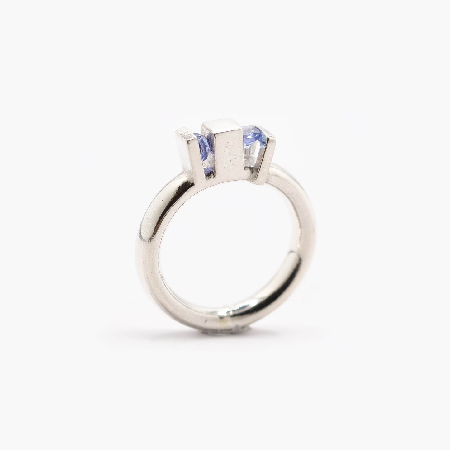 Une bague aux lignes architecturales,. Son anneau rond met en valeur deux volumes verticaux qui accueillent deux tanzanites bleues.