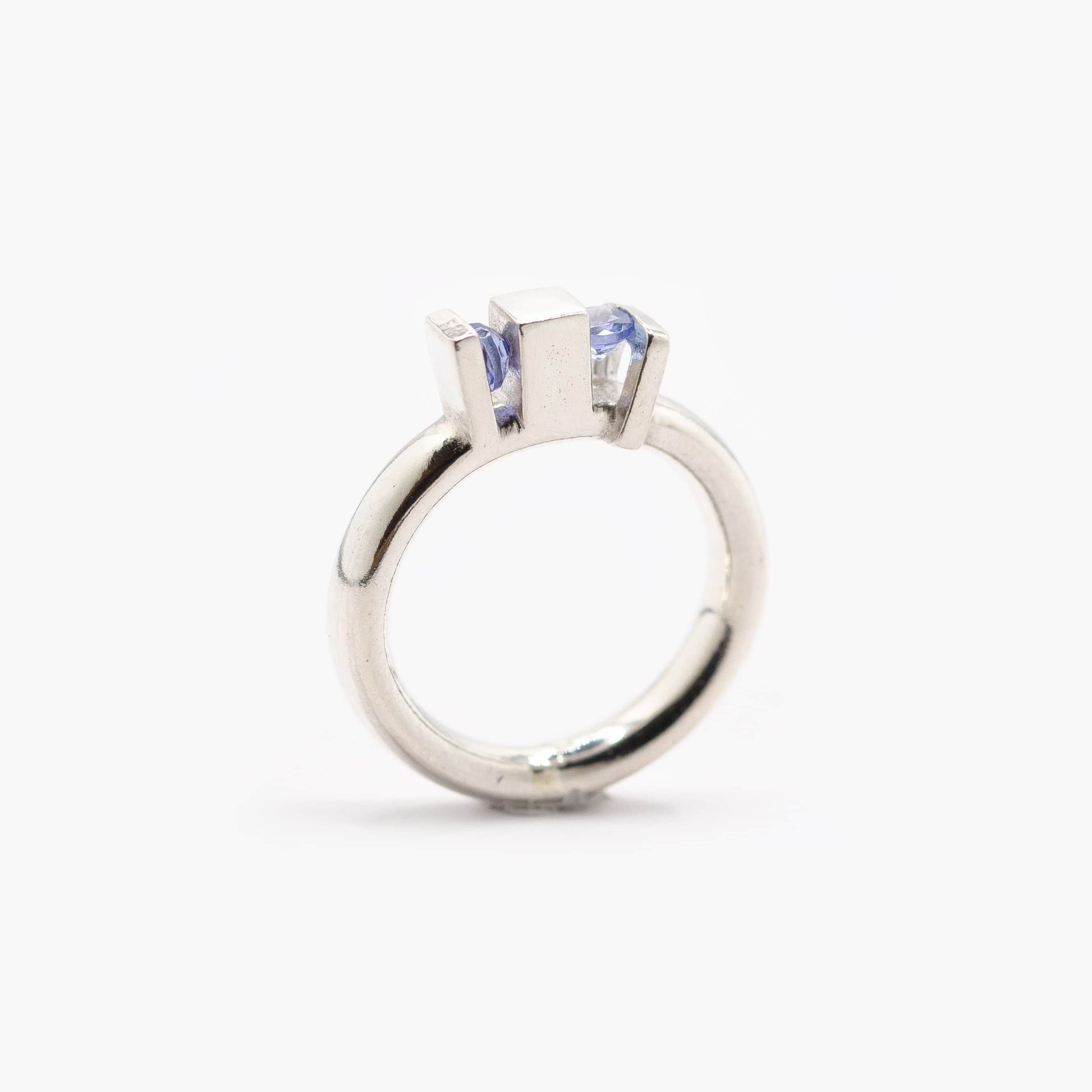 Une bague aux lignes architecturales,. Son anneau rond met en valeur deux volumes verticaux qui accueillent deux tanzanites bleues.