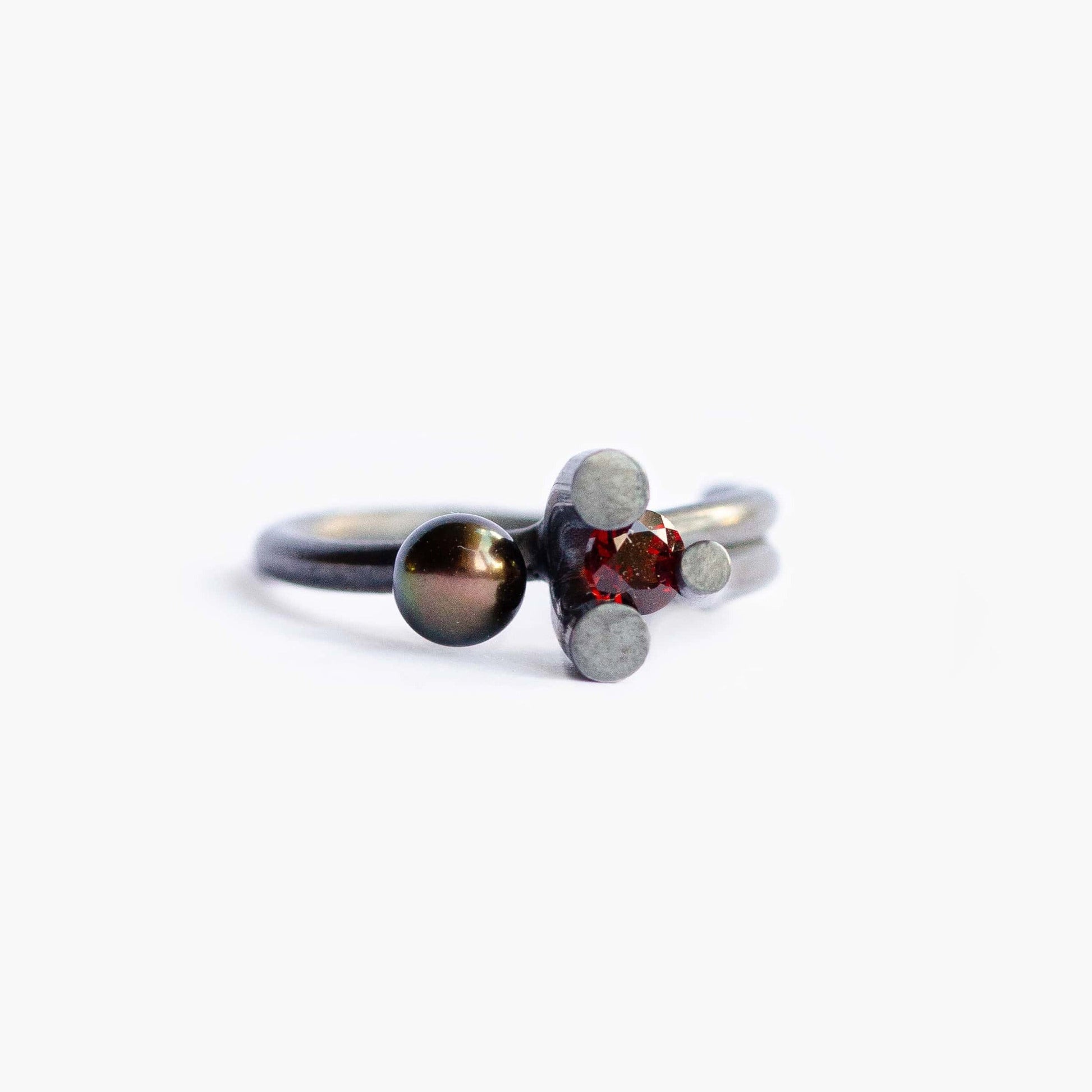 Bague organique et sculpturale en ’argent oxydé, l’éclat sombre de la perle noire et la couleur intense du grenat donne à cette bague une présence contemporaine.