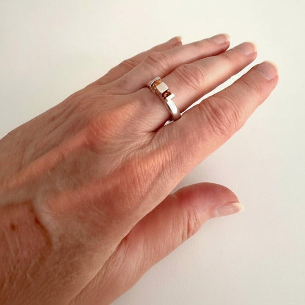 Bague géométrique en argent avec anneau rond et volumes architecturaux, sertie de deux grenats spessartite aux teintes orange lumineuses. Bijou signé Stefanie Verhoef, artiste d'origine néerlandaise-danoise.