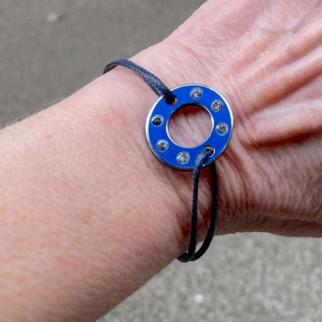 Bracelet Ready-Made, rondelle en  aluminium bleu et six saphirs blancs. bijou upcyclé inspiration moto, présenté sur lien de coton réglable. Détail, bijou porté.