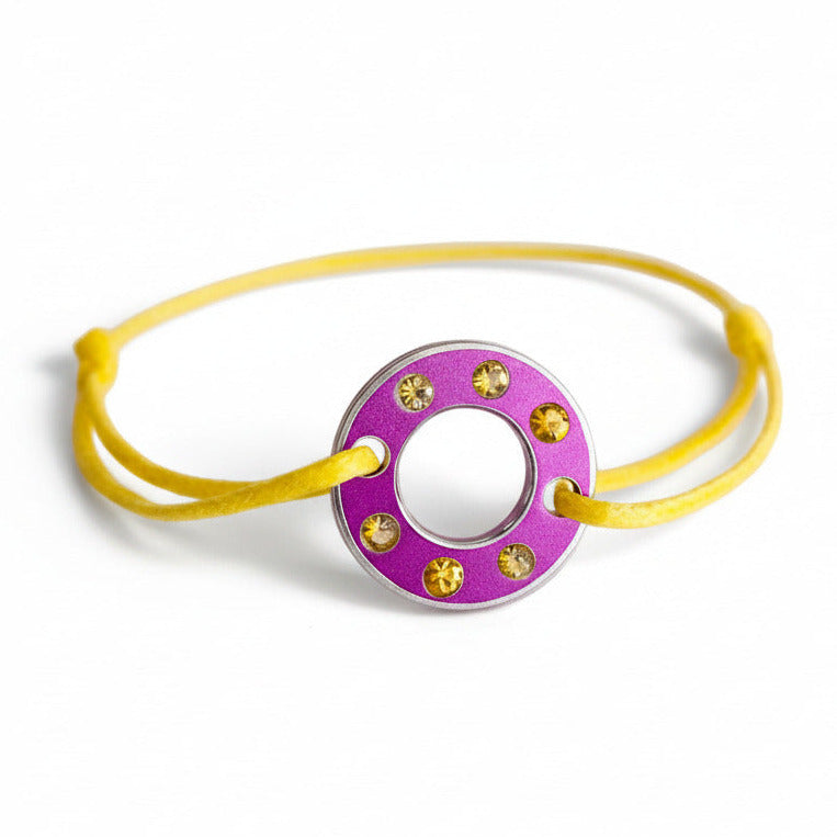 Bracelet Ready-Made composé d'une rondelle en aluminium violet sertie de  six saphirs jaunes facettés. Bracelet design et unisexe présenté sur lien de coton ciré. 