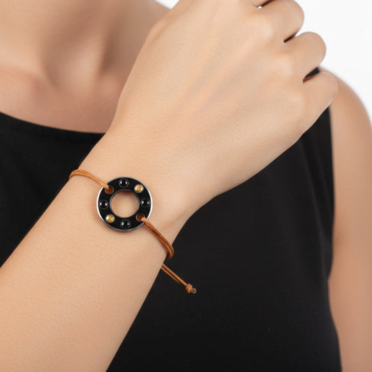 Bracelet Ready-Made en rondelle d'aluminium noir sertie de  quatre spinelles noirs et deux saphirs oranges. Un bracelet contemporain et unisexe présenté sur lien de coton ciré orange. Détail bijou porté.