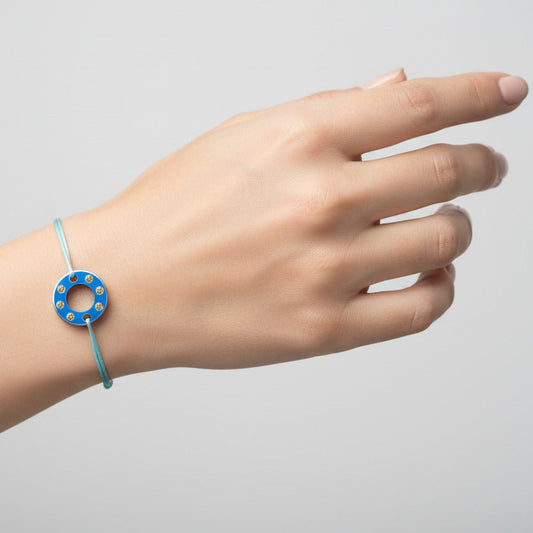 Bracelet Ready-Made petit modèle signé Charlotte Romer, rondelle en aluminium anodisé bleu sertie de six saphirs jaunes. Bijou upcyclé présenté sur un lien réglable en coton ciré. 