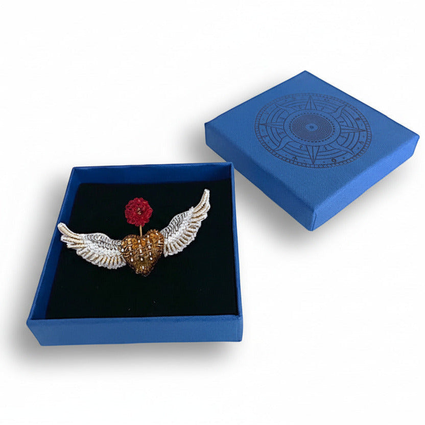 Prête à offrir, La broche Flying Angels est présentée dans un élégant écrin bleu signé Trovelore, accompagnée de sa notice explicative détaillant le travail de broderie et le savoir-faire artisanal.