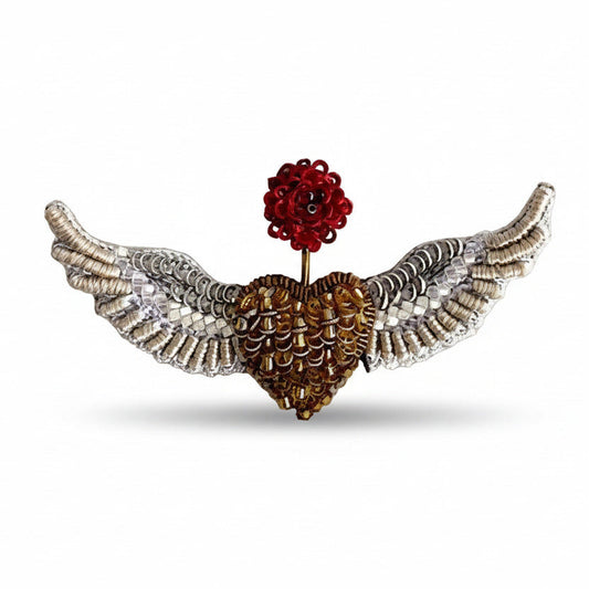 Broche en textile brodé et petites perles de verre. Représente un cœur doré en deux ailes déployées argenté, inspirée par les oiseaux et les anges. Une fleur rouge brodée sur le dessus symbolise le renouveau.