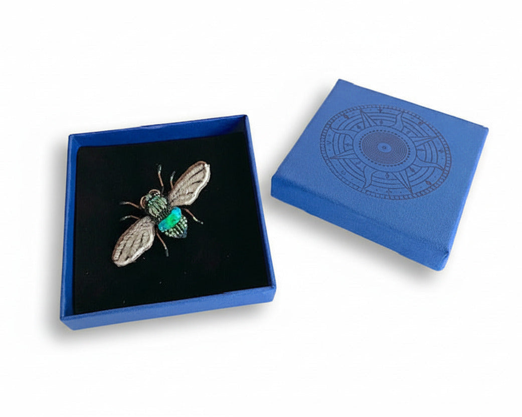 Prête à offrir, La broche Abeille des champs est présentée dans une boîte bleue signée Trovelore, accompagnée de sa notice explicative détaillant le travail de broderie et le savoir-faire artisanal.