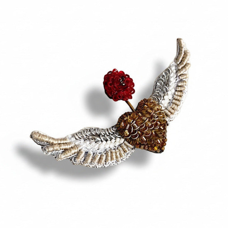 Broche en textile brodé,  représente un cœur doré en deux ailes déployées argenté, inspirée par les oiseaux et les anges. Une fleur rouge brodée sur le dessus symbolise le renouveau.