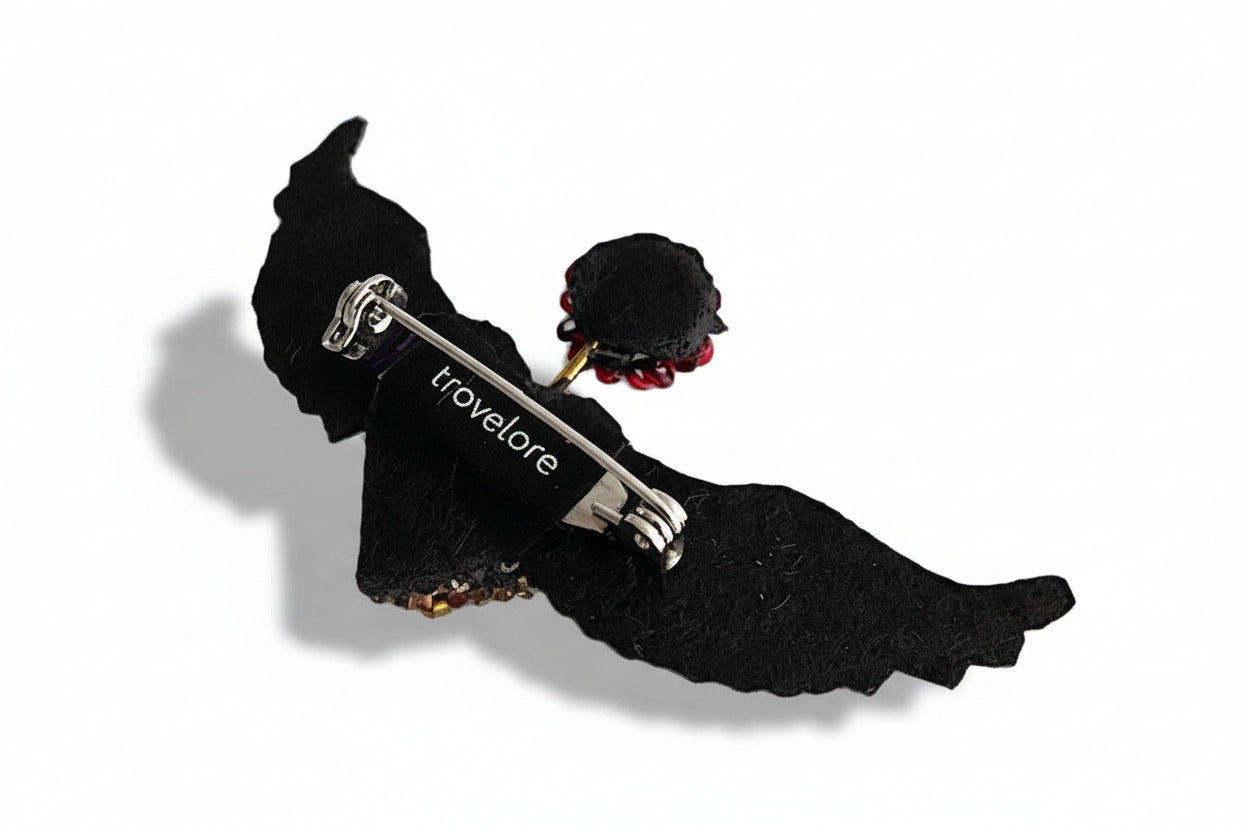 Broche en textile brodé,  représente un cœur doré en deux ailes déployées; Détail, vue envers, feutre noir et fermoir épingle.