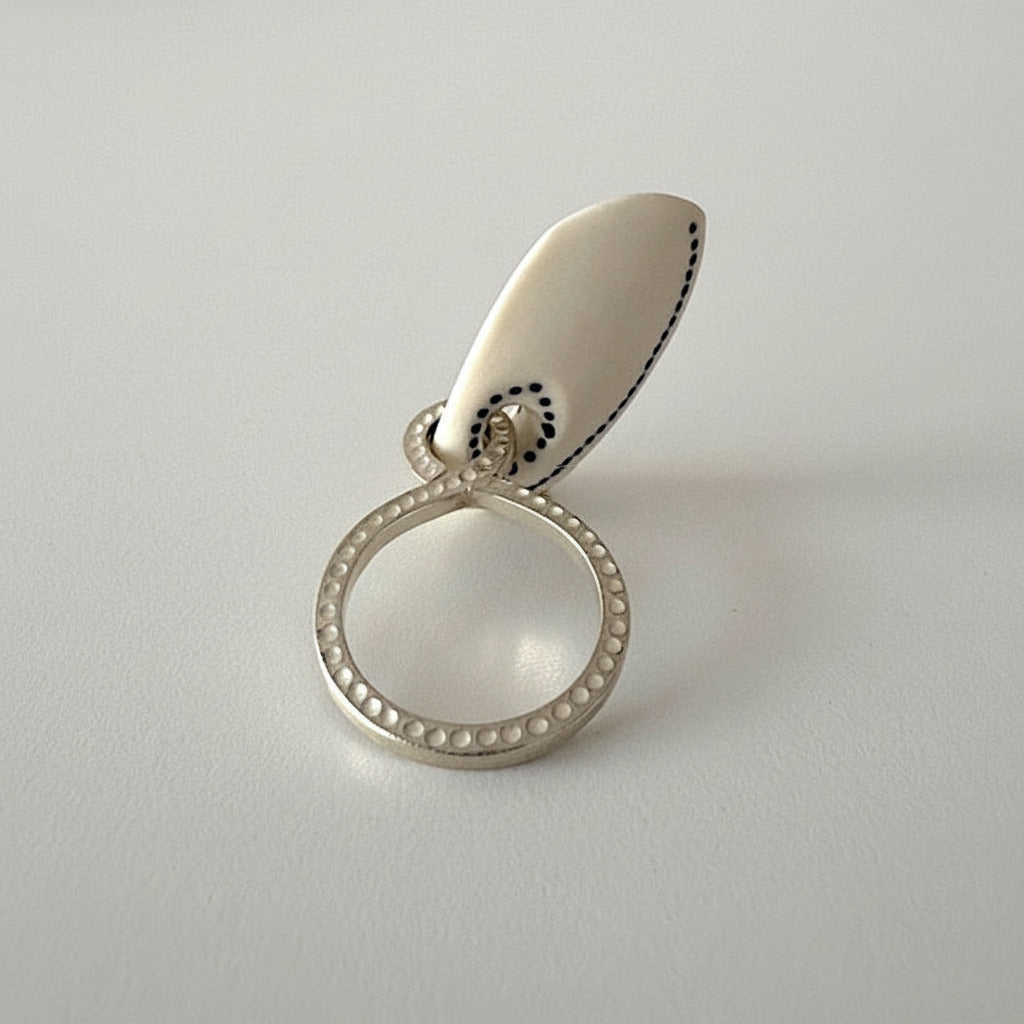 Bague design avec pampille en os sculpté tatoué de points noirs, associée à un anneau en argent texturé.