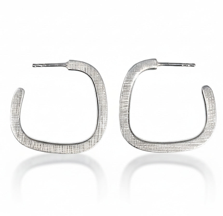 Boucles créoles géométriques en argent forgé en fil carré. Surfaces texturée, intérieur poli : un jeu subtil de lumière et de contraste. Une création contemporaine signée Anne Milbeau.