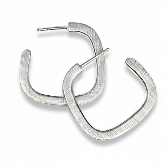 Boucles créoles contemporaines en argent forgé en fil carré. Surfaces striées, intérieur poli : un jeu subtil de lumière et de contraste. Une création minimaliste signée Anne Milbeau.