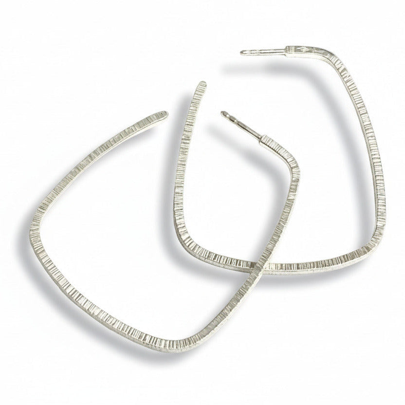 Grandes boucles créoles rectangulaires en argent forgé au fil carré, surfaces striées. Une création contemporaine signée Anne Milbeau. 