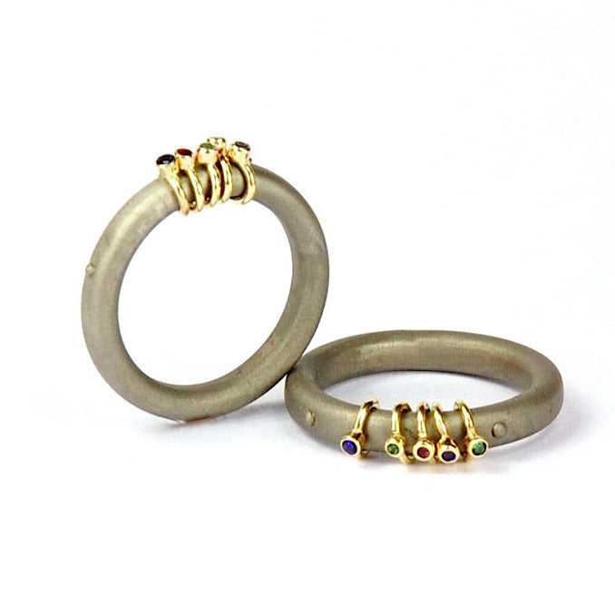 Bague acier inoxydable ornée de cinq  anneaux or jaune sertis de pierres colorées.  