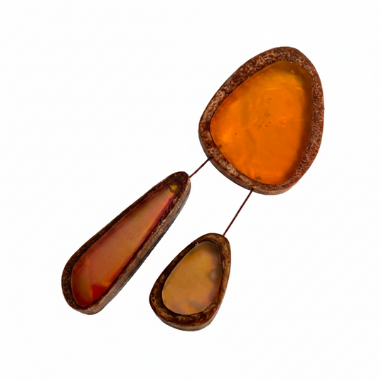 Broche en résine orange composée de trois éléments de différentes tailles,deux petits éléments sont reliés au plus grand par un cable rigide noir. fermeture aimant-fabrication-artisanale.